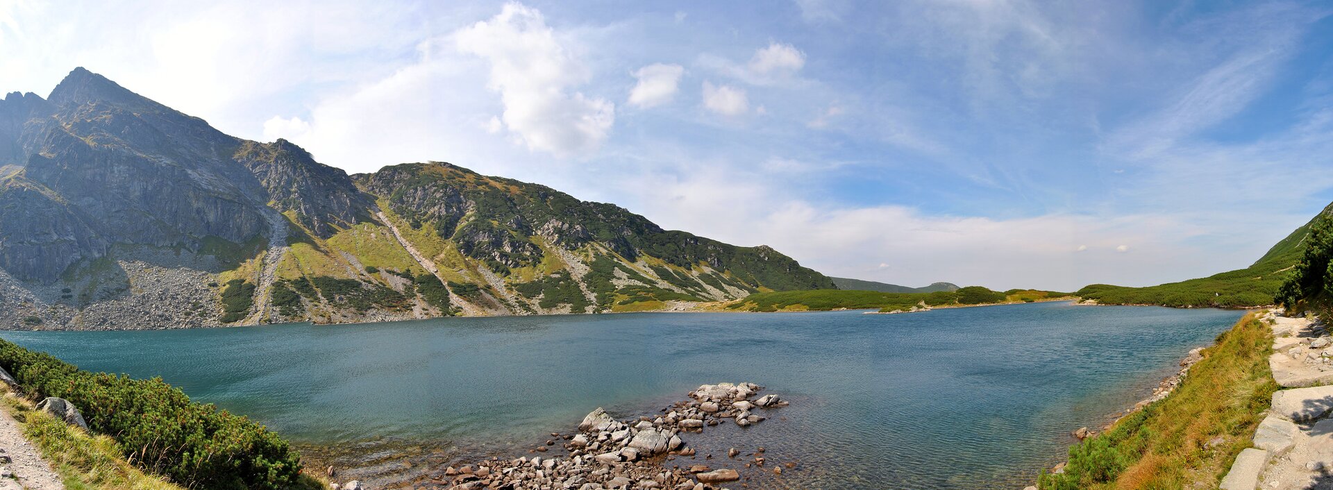 Na fotografii został ukazany krajobraz górski. Na środku znajduje się jezioro polodowcowe. Głazy rozmieszczone na jego brzegach są pokryte sinicami. Jezioro ma kształt owalny. Woda jest przezroczysta, o zabarwieniu szafirowym. Leżą w niej kamienie. Znajduje się na nim niewielka wysepka porośnięta kosodrzewiną. W dali widać góry. Niebo jest błękitne. 