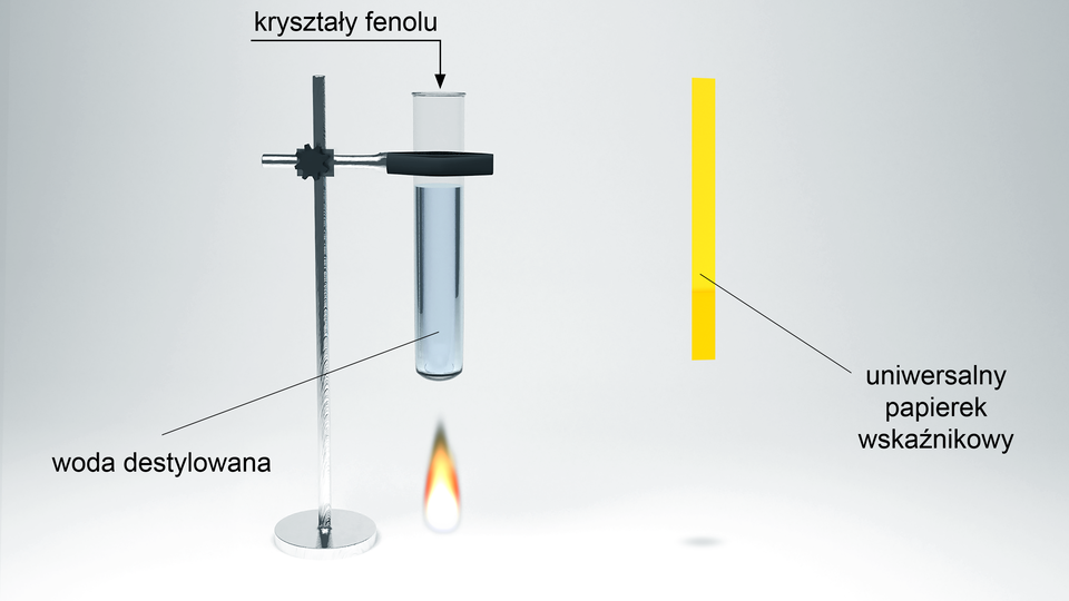 Ilustracja przedstawiająca statyw laboratoryjny z metalową łapą, w której umieszczono probówkę. W probówce znajduje się woda destylowana. Do probówki dodano kryształy fenolu. Pod probówką znajduje się palnik. Obok statywu znajduje się uniwersalny papierek wskaźnikowy w swoistym kolorze, to jest żółtym.