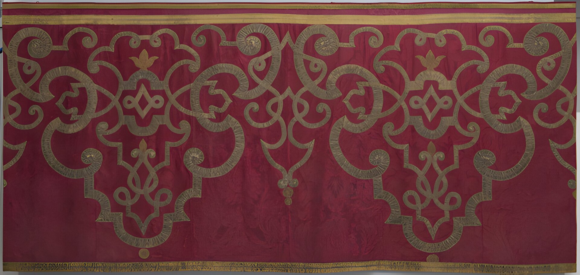 Na zdjęciu zaprezentowany został fragment czerwonego materiału, na którym wyszyte zostały ornamenty, niegdyś prawdopodobnie w złotym kolorze, jednakże wraz z upływem czasu kolory wyblakły i teraz są beżowe.