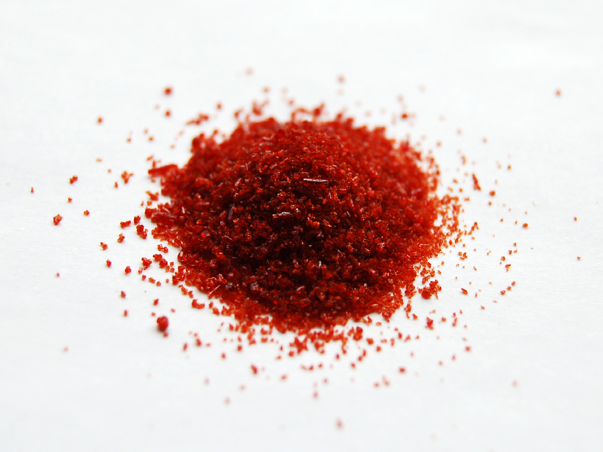 Ilustracja przedstawia czerwony proszek rozsypany na blacie.