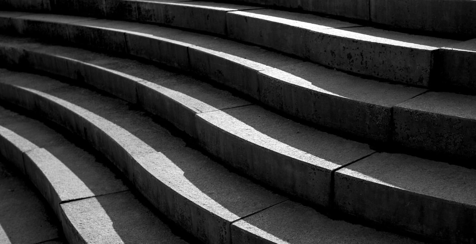 Zdjęcie wykonane z poziomu niewysokiego patrzącego, ujęcie z boku i przedstawia kamienne schody. Mają ciekawy kształt, przypominający łagodną falę, brzegi stopni są częściowo oświetlone słońcem. 