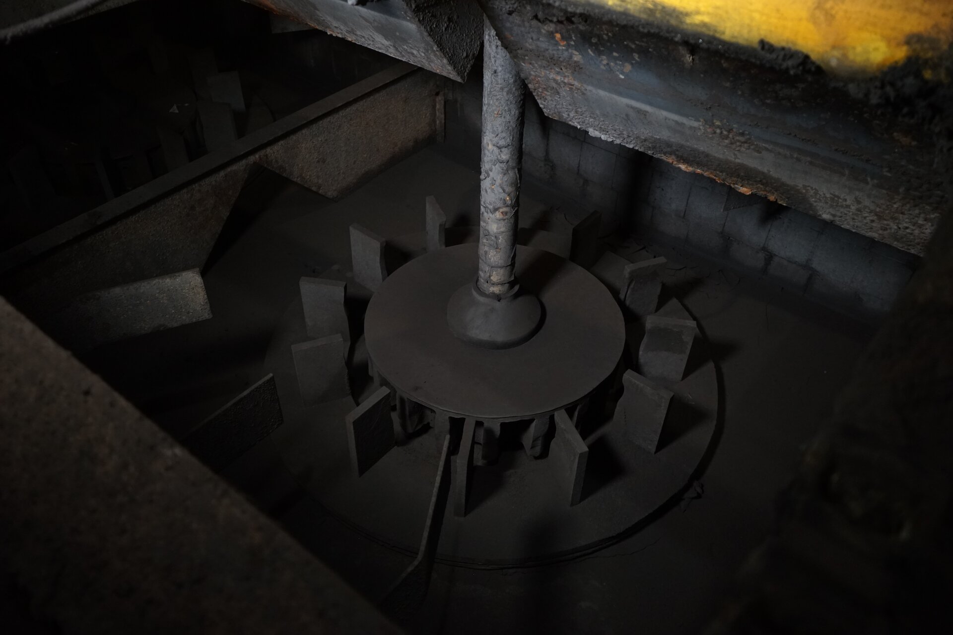 Zdjęcie przedstawia wirnik zabudowany statorem i otoczony uspokajaczami. Elementy maszyny flotacyjnej znajdują się na dnie pustej komory flotownika. Wirnik zamontowany jest w pionowo wydrążonym wale, wewnątrz komory mieszalnikowej. Wirnik zabudowany jest statorem o walcowatym kształcie. Wirnik umożliwia mieszanie zawartości komory, jej równomierne napowietrzenie oraz przepływ mętów w pożądanym kierunku, to jest poprzez stator. Wspomniany stator to nieruchomy element, którym zabudowany jest wirnik. Posiada on łopatki umocowane do poziomej płyty ustawionej powyżej dna przedziału roboczego oraz centralnie umieszczony otwór. Stator ukierunkowuje ruch wirowy cieczy w komorze nadawany przez wirnik. Dookoła opisanych elementów konstrukcyjnych rozmieszczone są promieniście na planie okręgu uspokajacze. Stanowią je nieduże, zorientowane pionowo blaszki. Poniżej zdjęcia znajduje się przycisk multimedialny z nagraniem audio. Treść nagrania jest zgodna z tytułem zdjęcia.