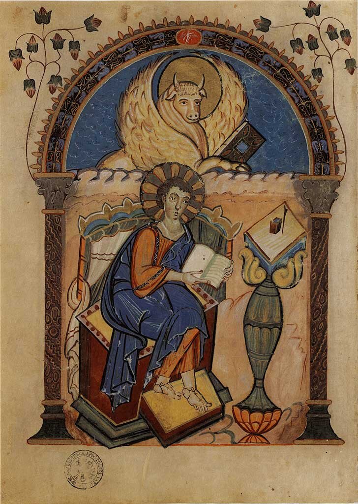 Iluminacja średniowiecznego manuskryptu ukazująca ewangelistę siedzącego na tronie i piszącego w księdze. Postać ma aureolę i ubrana jest w szaty w odcieniach błękitu i ochry. Nad nim, w półkolistej arkadzie, widnieje symbol ewangelisty – uskrzydlony wół, trzymający księgę. Scenę otaczają dekoracyjne kolumny, roślinne ornamenty i intensywne kolory na tle postarzonego pergaminu.