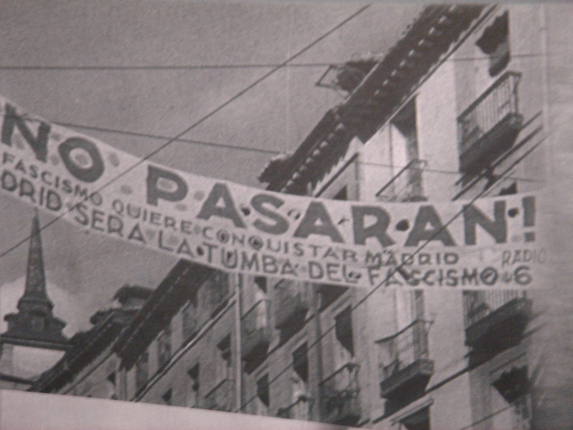 Zdjęcie przedstawia rozwieszony między budynkami baner z napisem No pasarán!