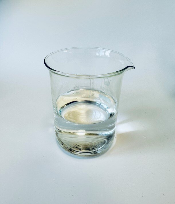 Zdjęcie przedstawia szklane naczynie z przezroczystą cieczą - acetonem.
