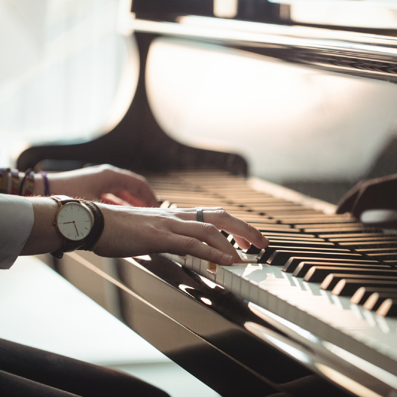 Ilustracja przedstawia pianino. Na klawisze pianina naciskają kobiece palce. Na środkowym palcu prawej ręki, kobieta ma pierścionek. Na nadgarstkach, nałożone ma liczne bransoletki. Na prawej dłoni, znajduje się zegarek.
