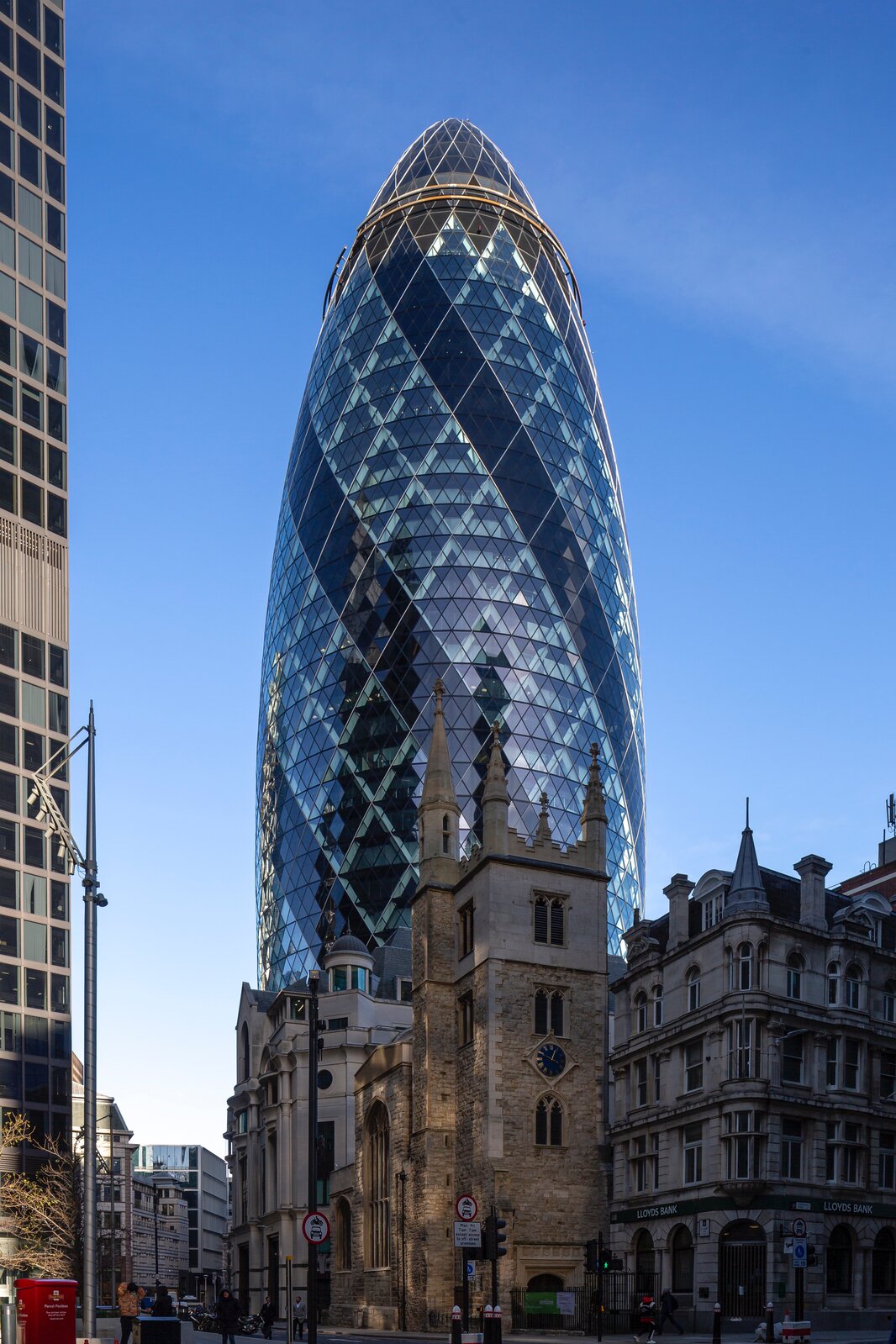 Zdjęcie przedstawia fragment dzielnicy finansowej w Londynie z wieżowcem 30 St Mary Axe, nazywanym The Gherkin, czyli Ogórek lub Swiss Re. Na pierwszym planie widoczne są niskie kamienice oraz zabytkowy kościół.  