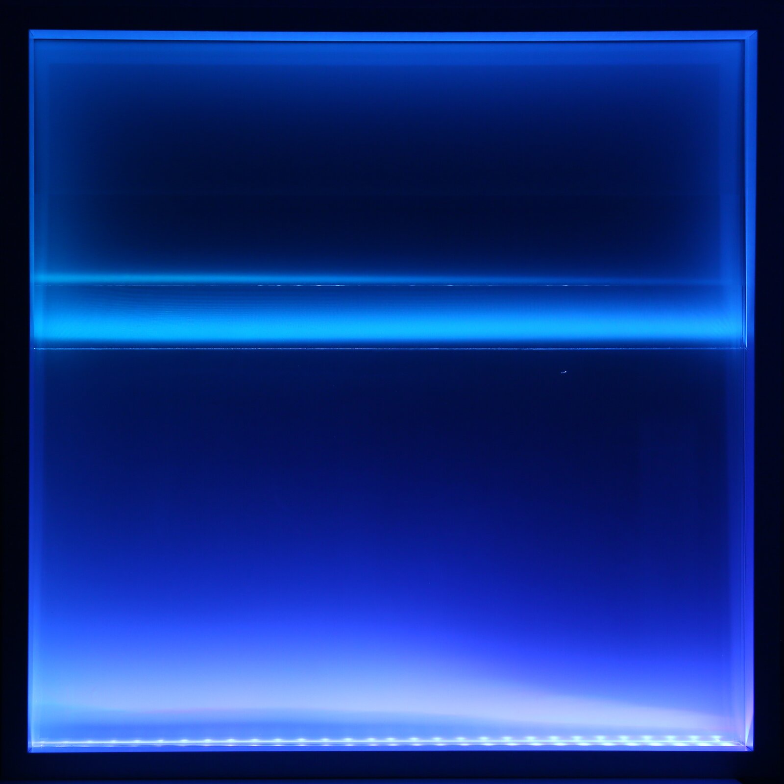 Ilustracja przedstawia pracę Agnieszki Majak „(Po)widok1‑dom”. Jest instalacją ukazującą kwadratową, niebieską powierzchnię, oświetloną białymi lampami. Poziome pasy światła lamp tworzą łagodne przejścia od niebieskiej do białej barwy.