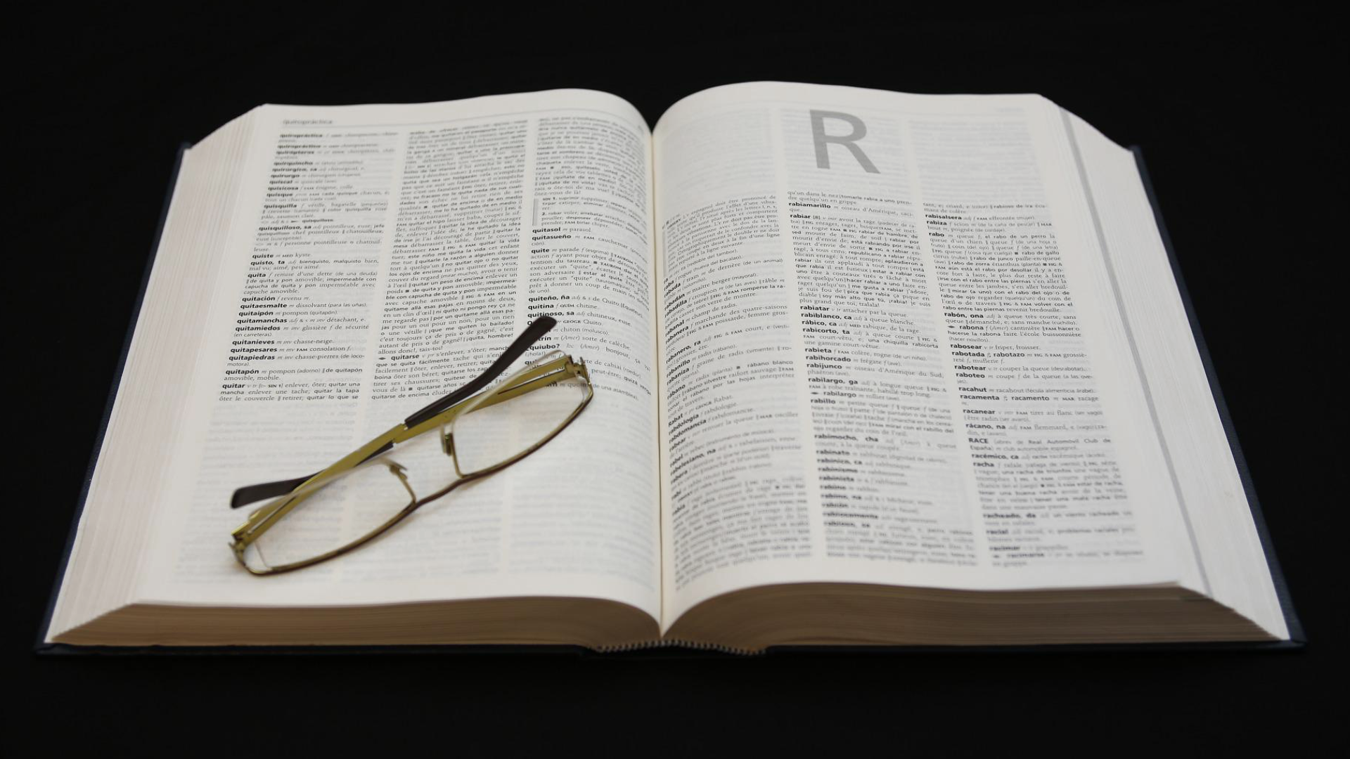 Zdjęcie przedstawia słownik otwarty na literze R. Na słowniku leżą złożone okulary.