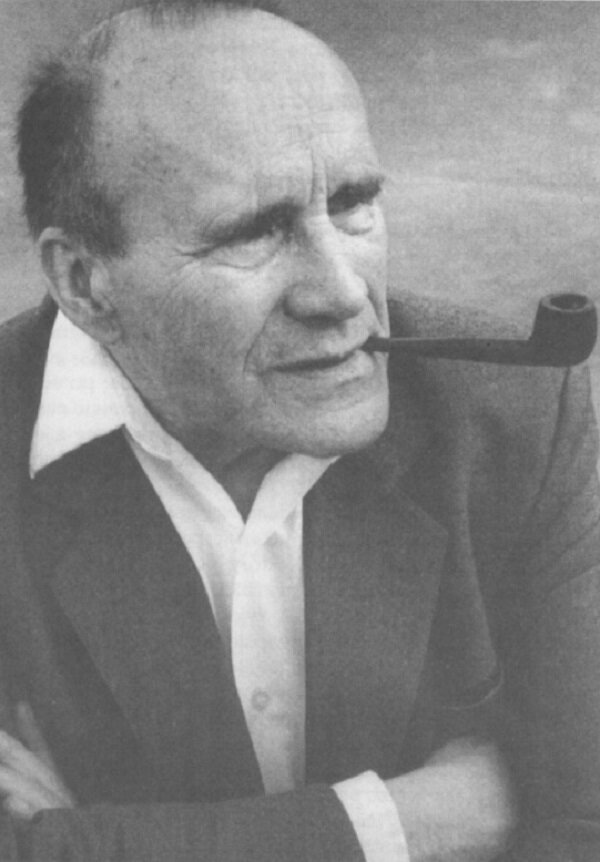 Czarno‑biały portret Jana Józefa Szczepańskiego. Starszy mężczyzna o wysokim czole i siwych włosach patrzy w bok, trzymając w ustach fajkę. Ma na sobie ciemną marynarkę i jasną koszulę z rozpiętym kołnierzykiem.
