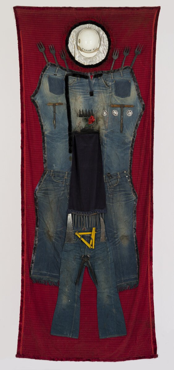 Ilustracja przedstawiająca dzieło autorstwa Władysława Hasiora pt. „Sztandar pracy”. Przedstawia on czarne robocze ubranie, kask oraz narzędzia na czerwonym materiale.