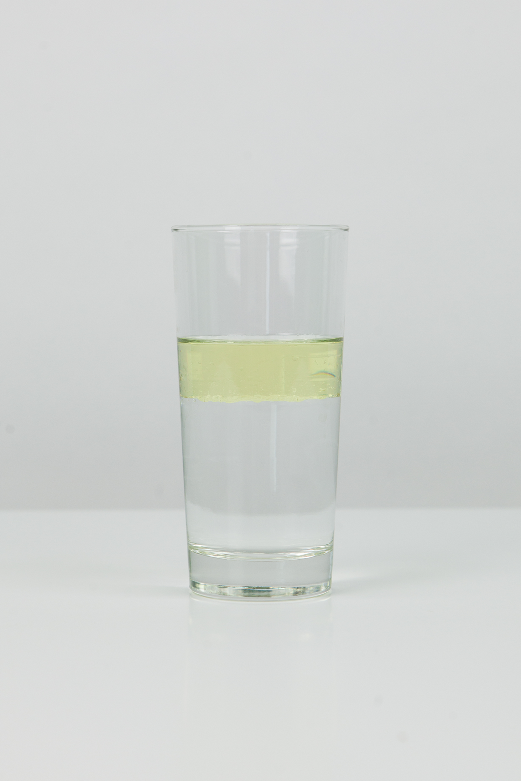 Mieszanina oleju i wody w szklance. Olej tworzy wyraźną, żółtą warstwę na powierzchni wody.