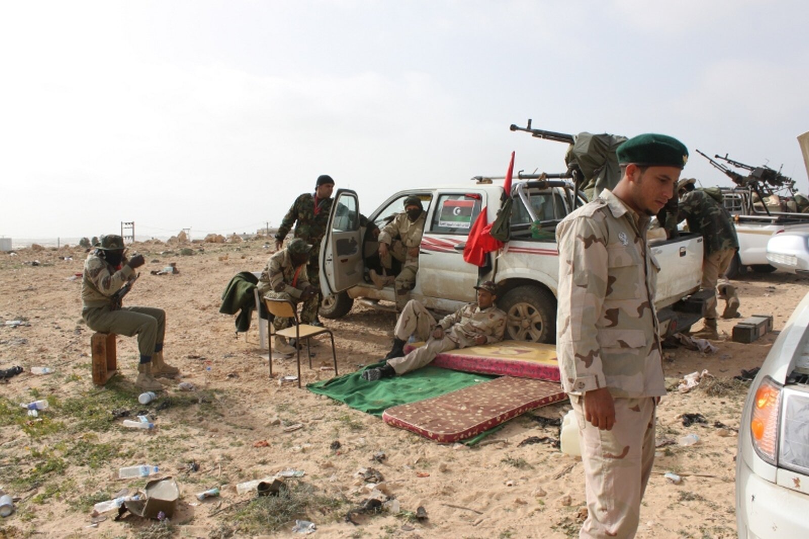 Zdjęcie przedstawia grupę mężczyzn w mundurach obok samochodów terenowych, na których zainstalowano karabiny maszynowe. Teren pustynny.
