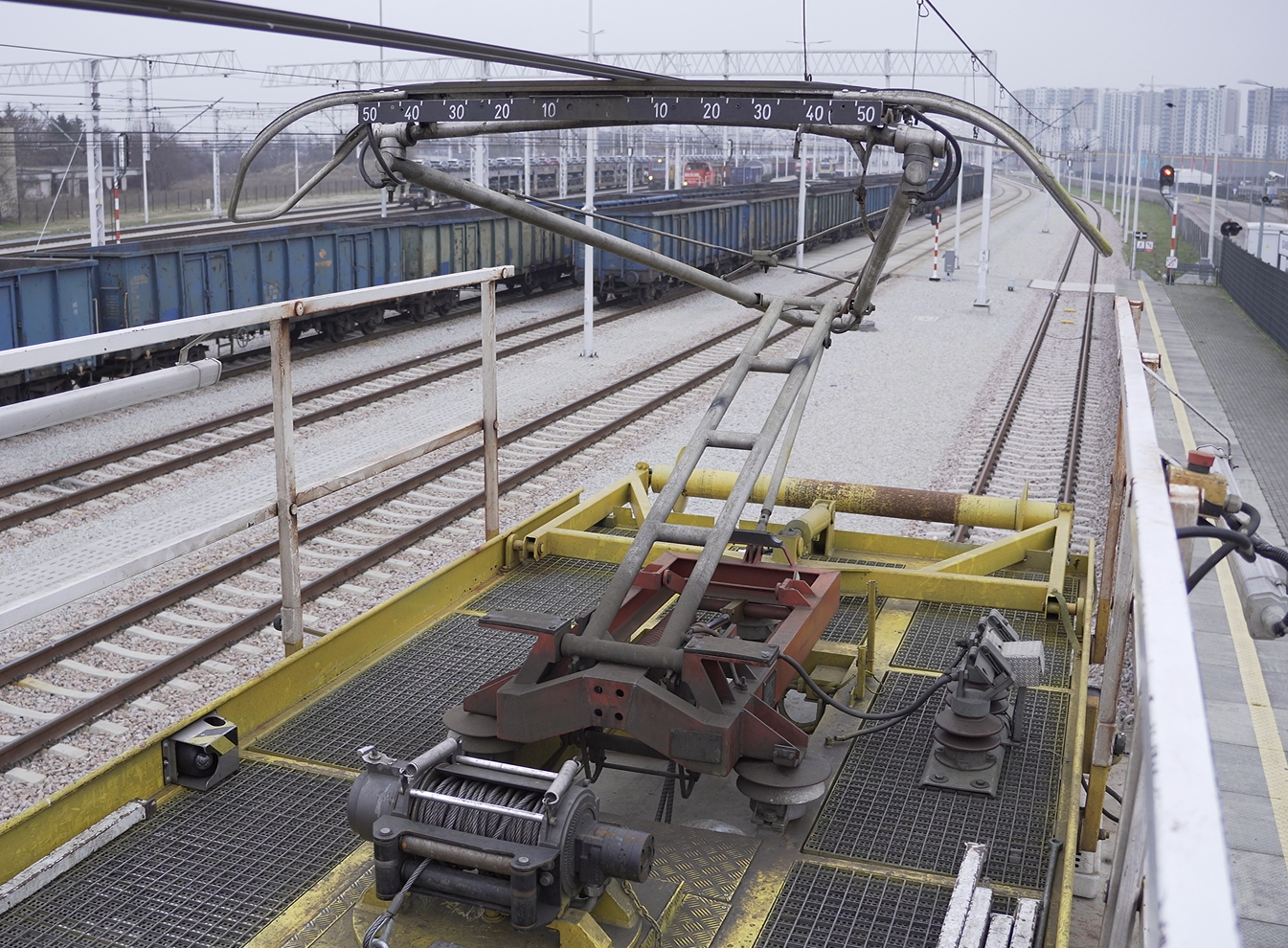 Zdjęcie obrazuje przejazd inspekcyjny. Widoczny jest na pierwszym planie odbiornik prądu na dachu wagonu diagnostyczno pomiarowego. Wagon stoi na torze, w tle widać wagony towarowe stojące na równoległych torach. Odbiornik prądu dotyka przewodu trakcyjnego.