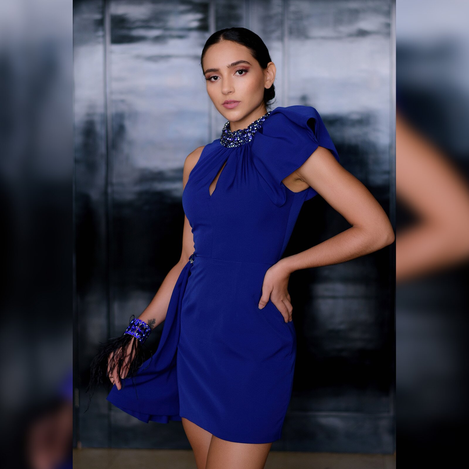 Zdjęcie przedstawia kobietę ubraną w chabrową sukienkę ozdobioną pod szyją niebieskimi koralikami.  