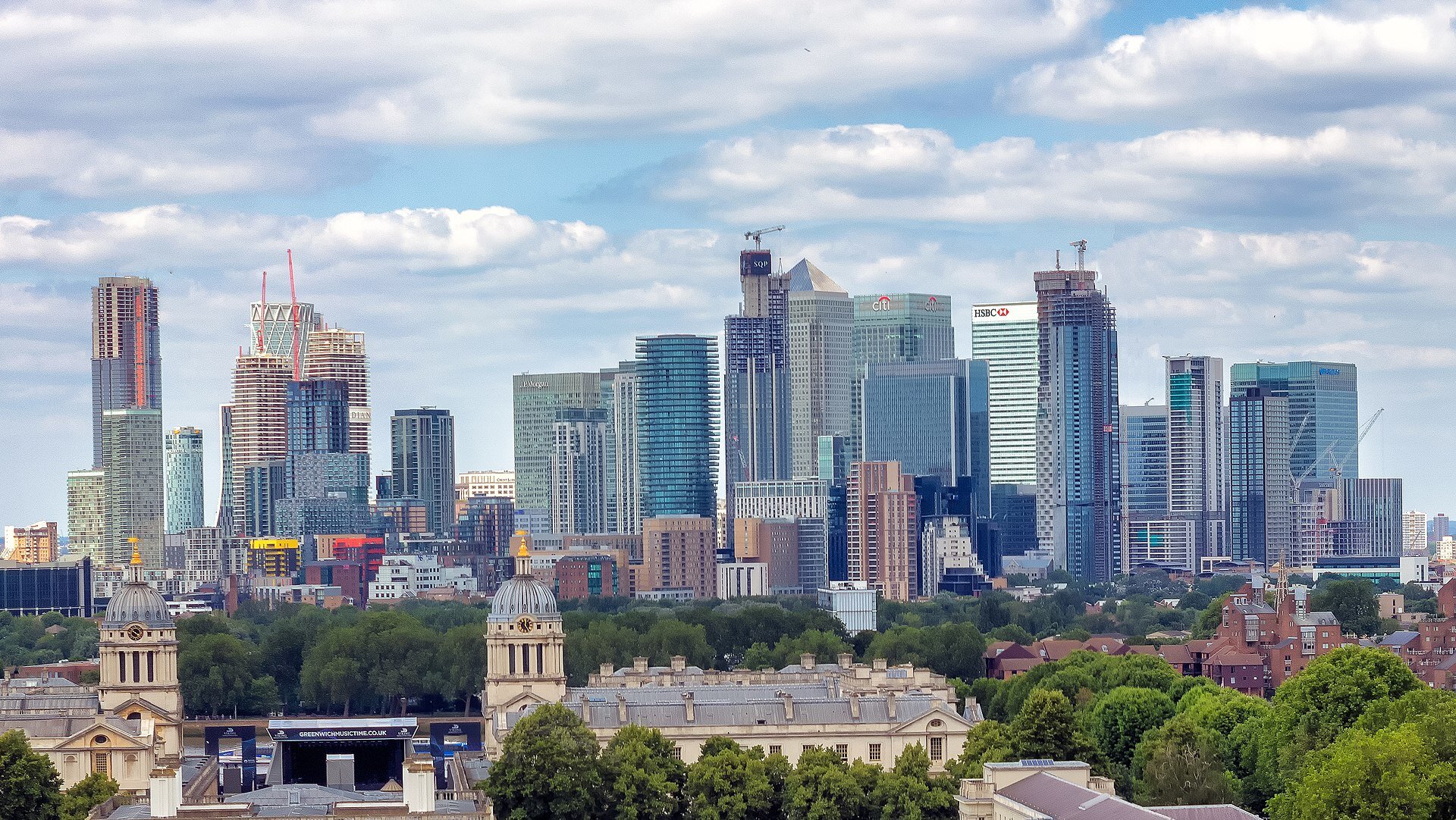 Fotografia kilkudziesięciu szklanych drapaczy chmur. Na pierwszym planie niższa zabudowa, drzewa.