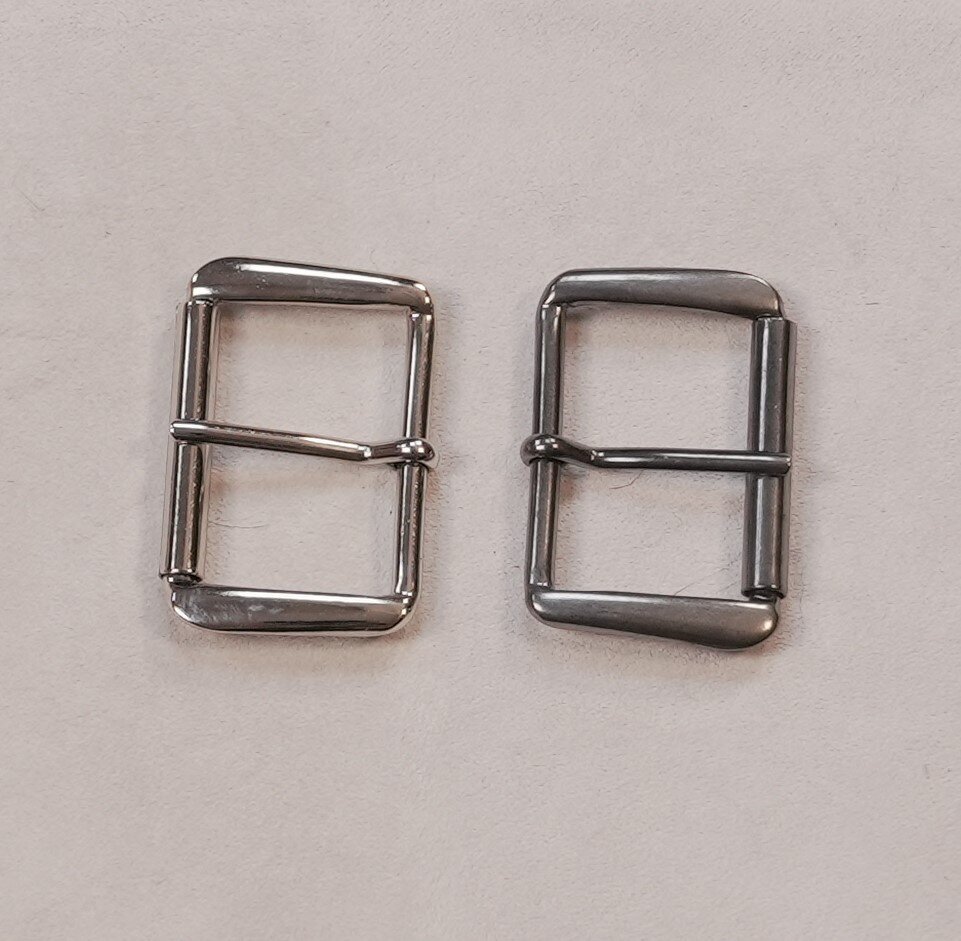 Na zdjęciu widoczne są dwie metalowe klamry. Składają się z prostokątnej ramy i elementu zapinającego.