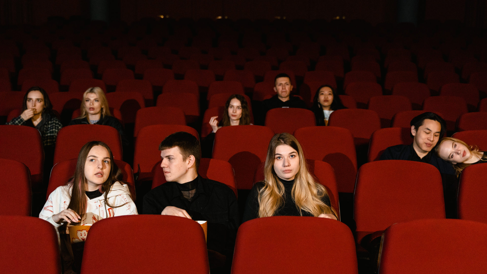 Zdjęcie przedstawia dziewczyny i chłopaków, którzy siedzą w fotelach w sali kinowej.