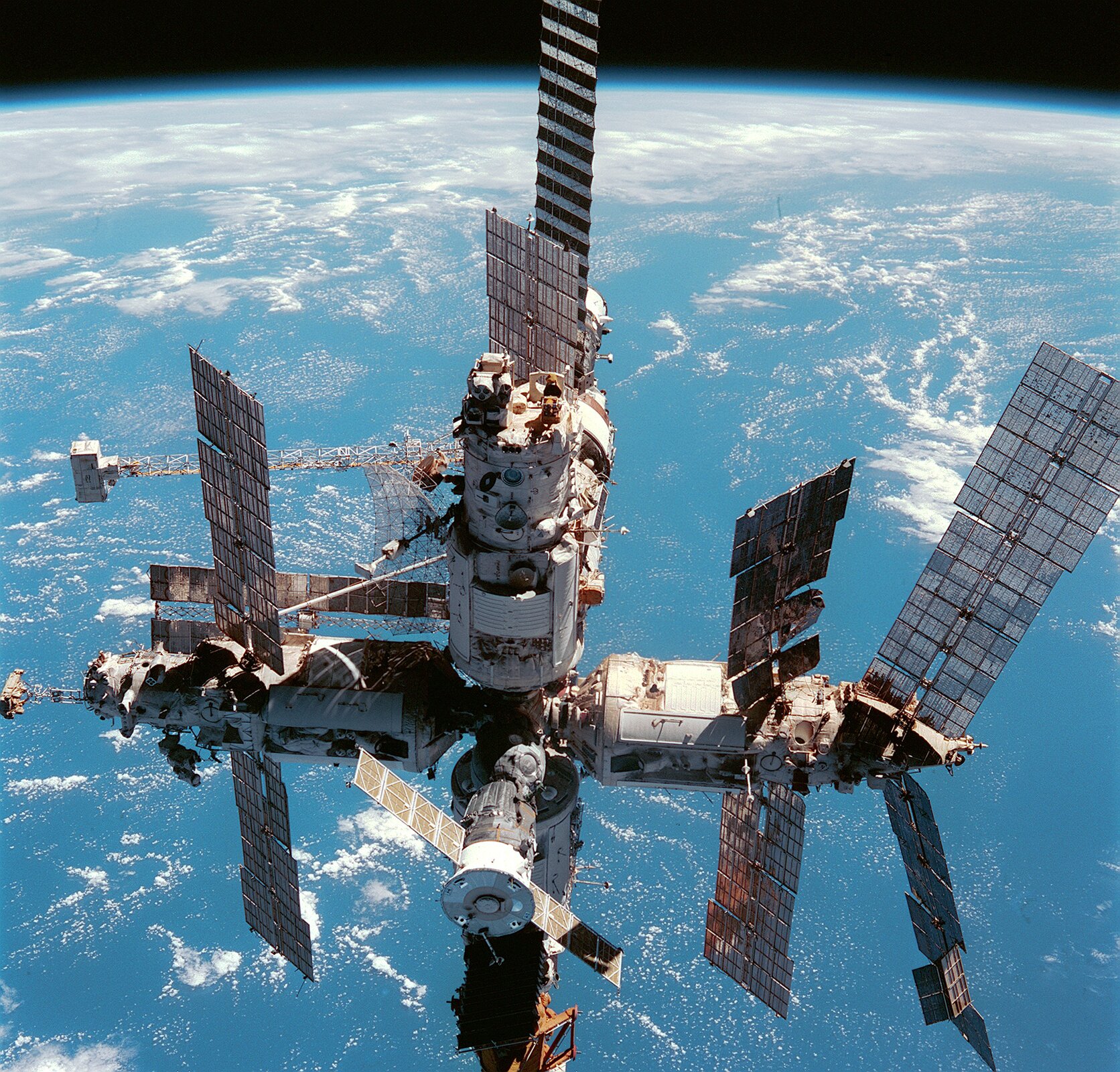 Zdjęcie przedstawia stację kosmiczną Mir na orbicie. Na pierwszym planie widoczna stacja kosmiczna, w tle kula ziemska.