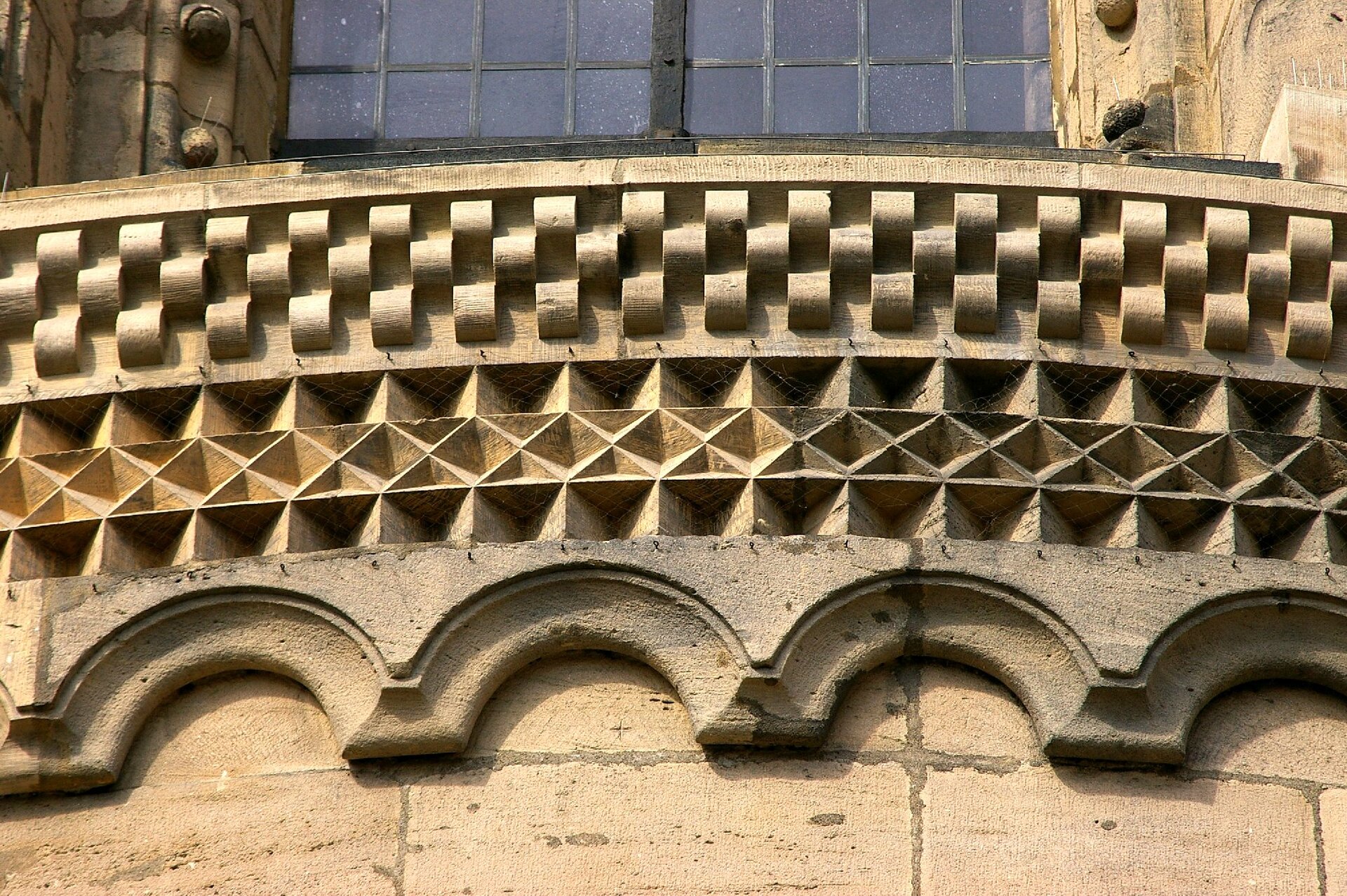 Zdjęcie przedstawia fryz, który wyrzeźbiony jest w różne geometryczne, symetryczne wzory, takie jak romby i kwadraty.