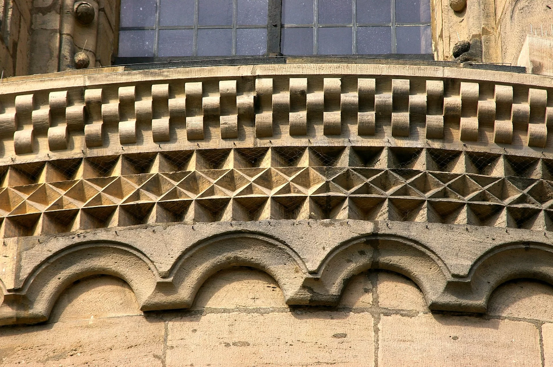 Zdjęcie przedstawia fryz, który wyrzeźbiony jest w różne geometryczne, symetryczne wzory, takie jak romby i kwadraty.