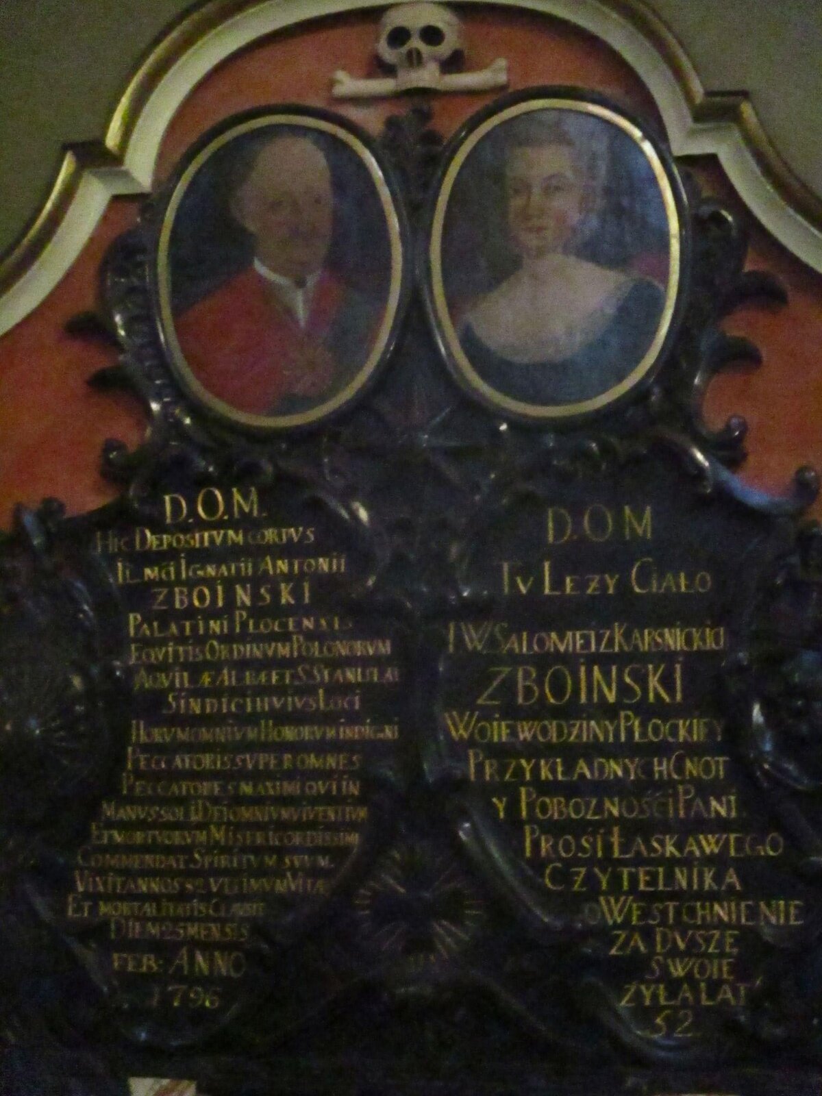 Ozdobna płyta z ozdobnym wykończeniem u góry. Pod nim czaszka z poziomą kością pod szczęką. Niżej dwa portrety na owalnym tle. Po lewej przedstawiony jest łysawy mężczyzna z wąsem, w średnim wieku, ubrany w białą koszulę i czerwoną marynarkę przez którą ma przewieszoną szarfę. Po prawej portret kobiety w średnim wieku z dość krótkimi kręconymi włosami, w ciemnej sukni z dużym białym kołnierzem z koronką. Niżej, na czarnym tle dwa teksty. Po lewej w kolumnie złotymi drukowanymi literami w kilkunastu wierszach zapisano tekst po łacinie. Po prawej większymi również złotymi drukowanymi literami zapisano krótszy tekst w języku staropolskim. Oba teksty zaczynają się od skrótu D.O.M.