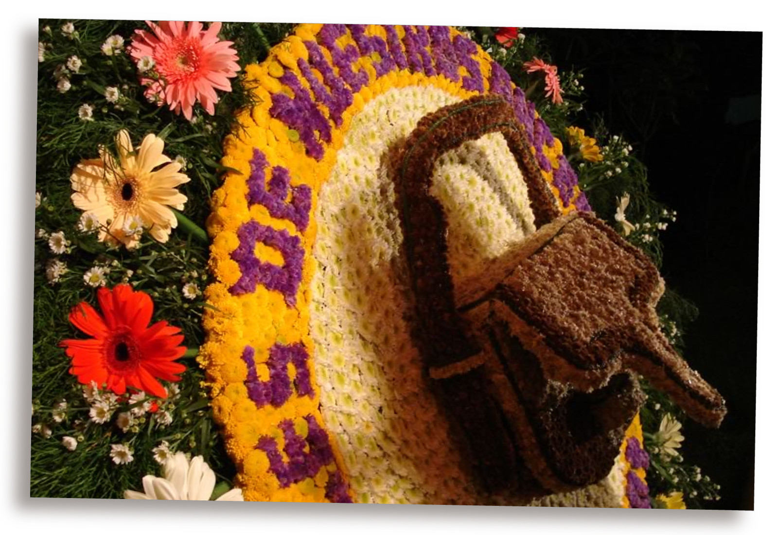 Zdjęcie przedstawia kobierzec ułożony z suszonych kwiatów. Składa się w napis oraz rzeźbę.