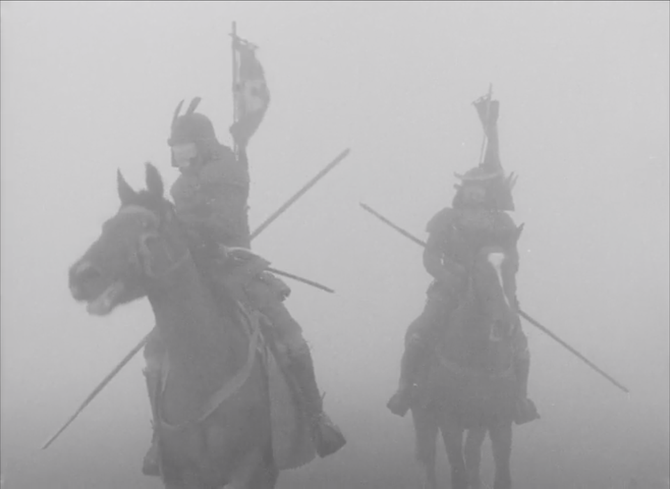 Czarno‑białe zdjęcie przedstawia dwóch samurajów na koniach. Są ubrani w samurajskie zbroje na głowach mają hełmy w ręku piki, a na plecach przymocowane chorągwie. Mężczyźni błądzą w gęstej mgle.