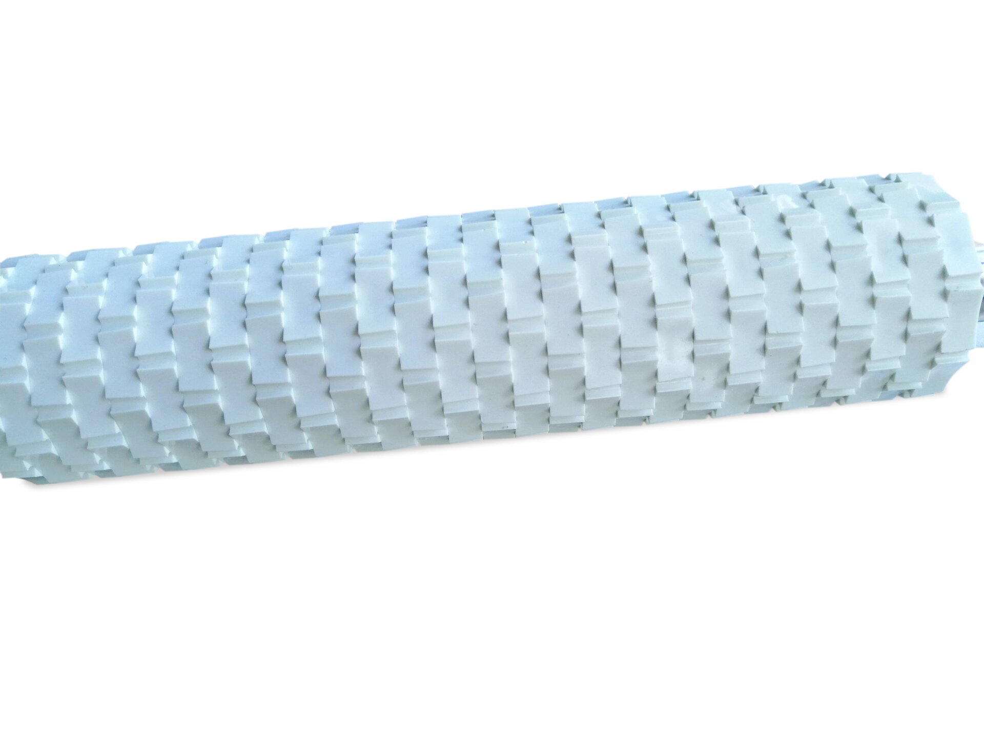 Zdjęcie przedstawia wałek dekoracyjny do rozwałkowywania mas cukrowych. Widoczny jest fragment białego wałka, którego powierzchnia pokryta jest wklęsłymi geometrycznymi ornamentami.