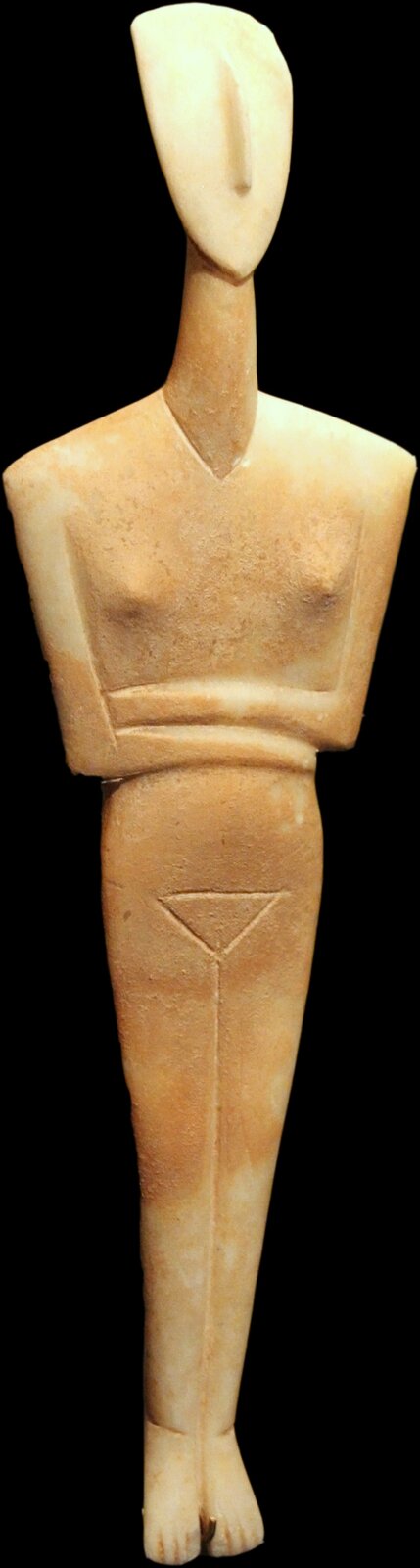 Ilustracja przedstawia  marmurową figurkę idola na czarnym tle. Ukazuje nagą postać kobiecą, stojącą w pozycji frontalnej, z rękami skrzyżowanymi pod piersiami. Ciało zostało uproszczone do geometrycznych, zredukowanych form: głowa jest w kształcie owalu, bez wyraźnych rysów twarzy (poza delikatnie zaznaczonym nosem), tors i nogi są wydłużone i smukłe, a ramiona ułożone symetrycznie. Stopy są skierowane w dół.  Powierzchnia figurki jest wygładzona.