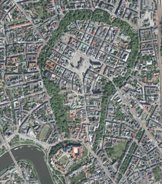 Ortofotomapa przedstawiająca historyczne centrum Krakowa z lotu ptaka. W górnej części widoczne jest Stare Miasto otoczone zielonym pierścieniem Plant. W jego centrum znajduje się prostokątny Rynek Główny, od którego odchodzą ulice tworzące zwartą sieć zabudowy. W dolnej części obrazu płynie Wisła. Nad jej lewym brzegiem znajduje się Wawel – zespół zabudowań zamkowych i katedry otoczony zielenią. Obszary poza Plantami zajmuje gęsta zabudowa miejska z ulicami, skwerami i pojedynczymi terenami zielonymi.