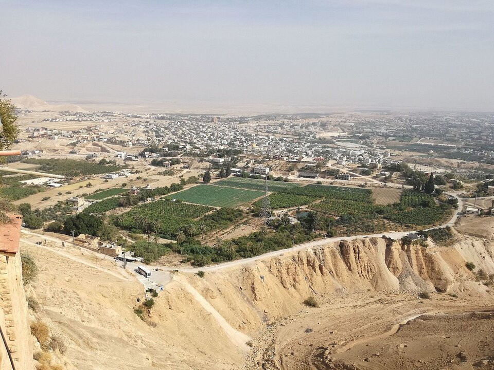 Zdjęcie przedstawia współczesną panoramę miasta widzianą z lotu ptaka. Miasto położone na piaszczystym, suchym terenie. Na pierwszym planie widać osuwisko piaskowe. Za nim na obrzeżach miasta duży kwartał zieleni obsadzony drzewami, krzewami i roślinnością. W oddali zabudowania miasta,  białe domy ciągną sie aż po horyzont. 