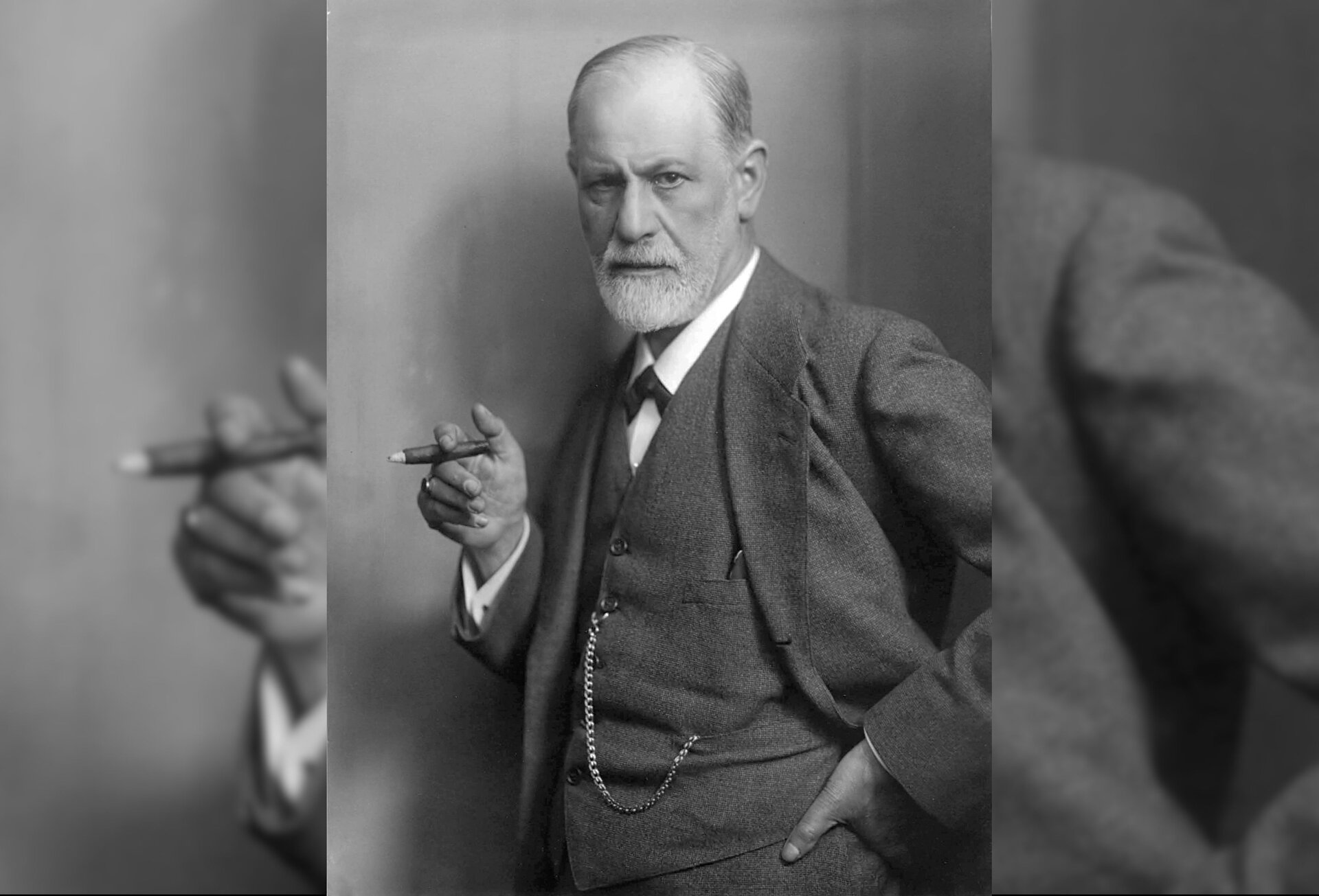 Zdjęcie przedstawia starszego mężczyznę. Jego twarz jest owalna, nos duży, oczy małe, osadzone blisko siebie. Mężczyzna ma krótkie, proste włosy zaczesane na prawą stronę. Mężczyzna ubrany jest w garnitur, kamizelkę, koszulę i krawatkę. Trzyma w prawej dłoni zapalone cygaro.