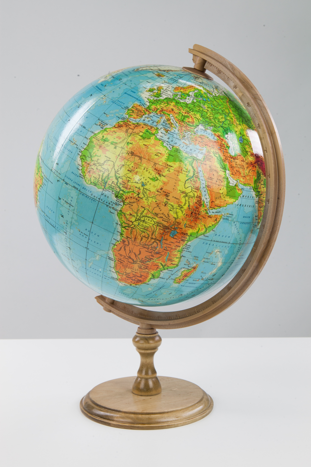 Fotografia przedstawia okrągły, pomarańczowo‑zielono‑niebieski globus. Pomniejszony model Ziemi w postaci kuli umieszczony jest na osi ustawionej pod kątem, przechodzącej przez jego środek i przez dwa punkty na jego powierzchni: biegun północny i biegun południowy. Globus jest tak obrócony, że widać na nim Europę i Afrykę.