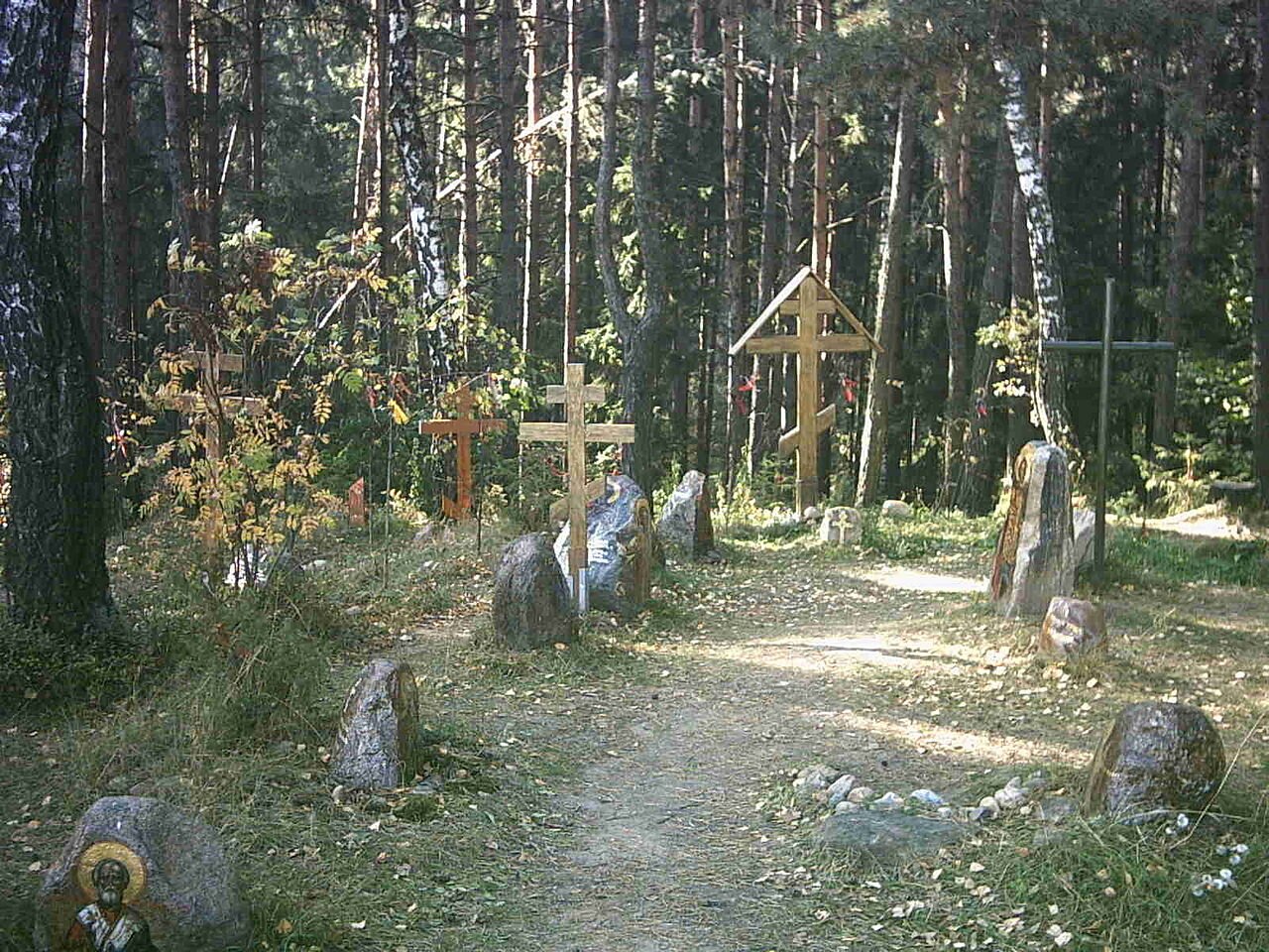 Zdjęcie przedstawia leśną polanę, na której leżą duże kamienie, a przy nich stoją drewniane krzyże prawosławne wbite w ziemie.