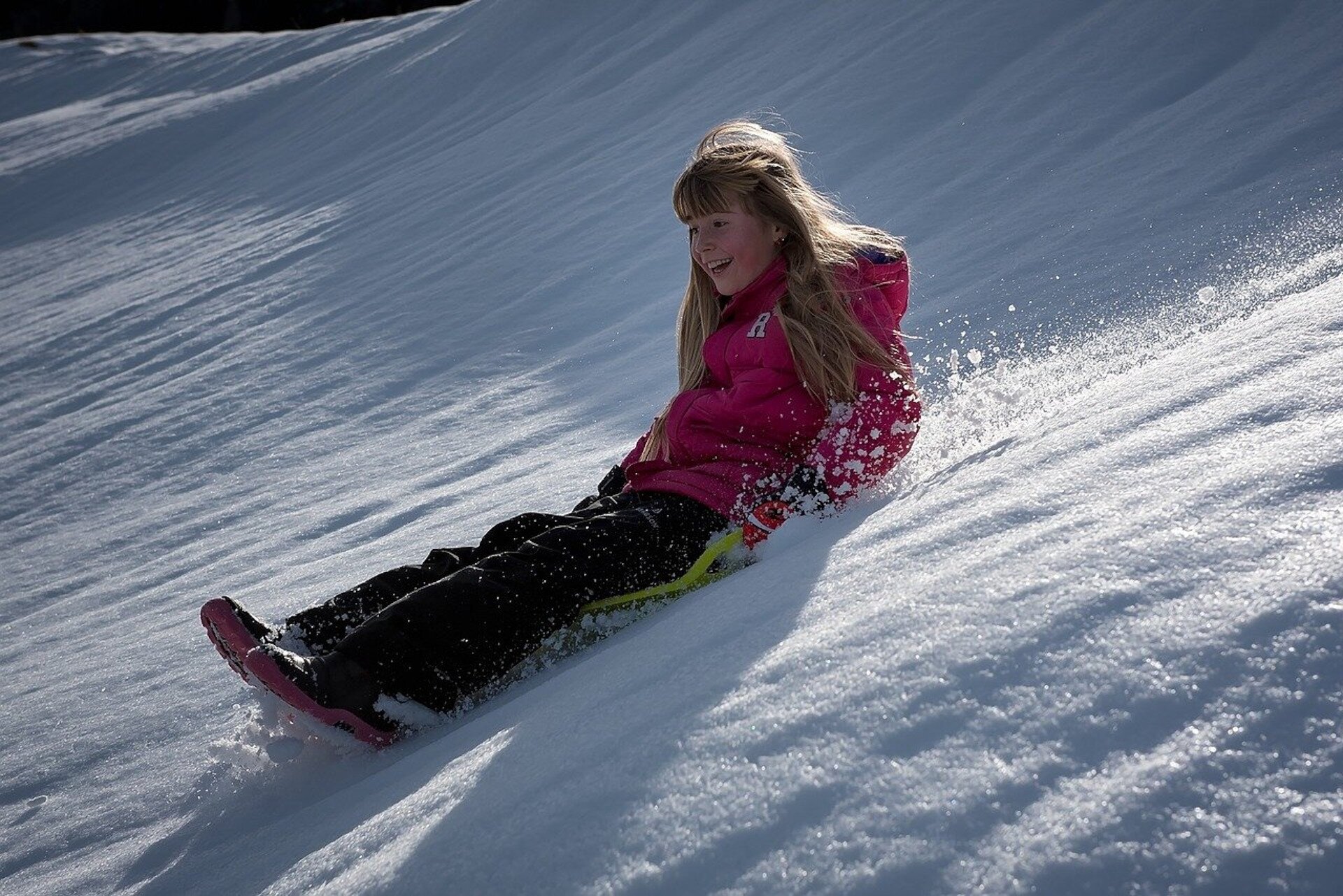 Rys. a. Na zdjęciu widać roześmianą dziewczynkę, która zjeżdża na plastikowym jabłuszku z ośnieżonej górki. 