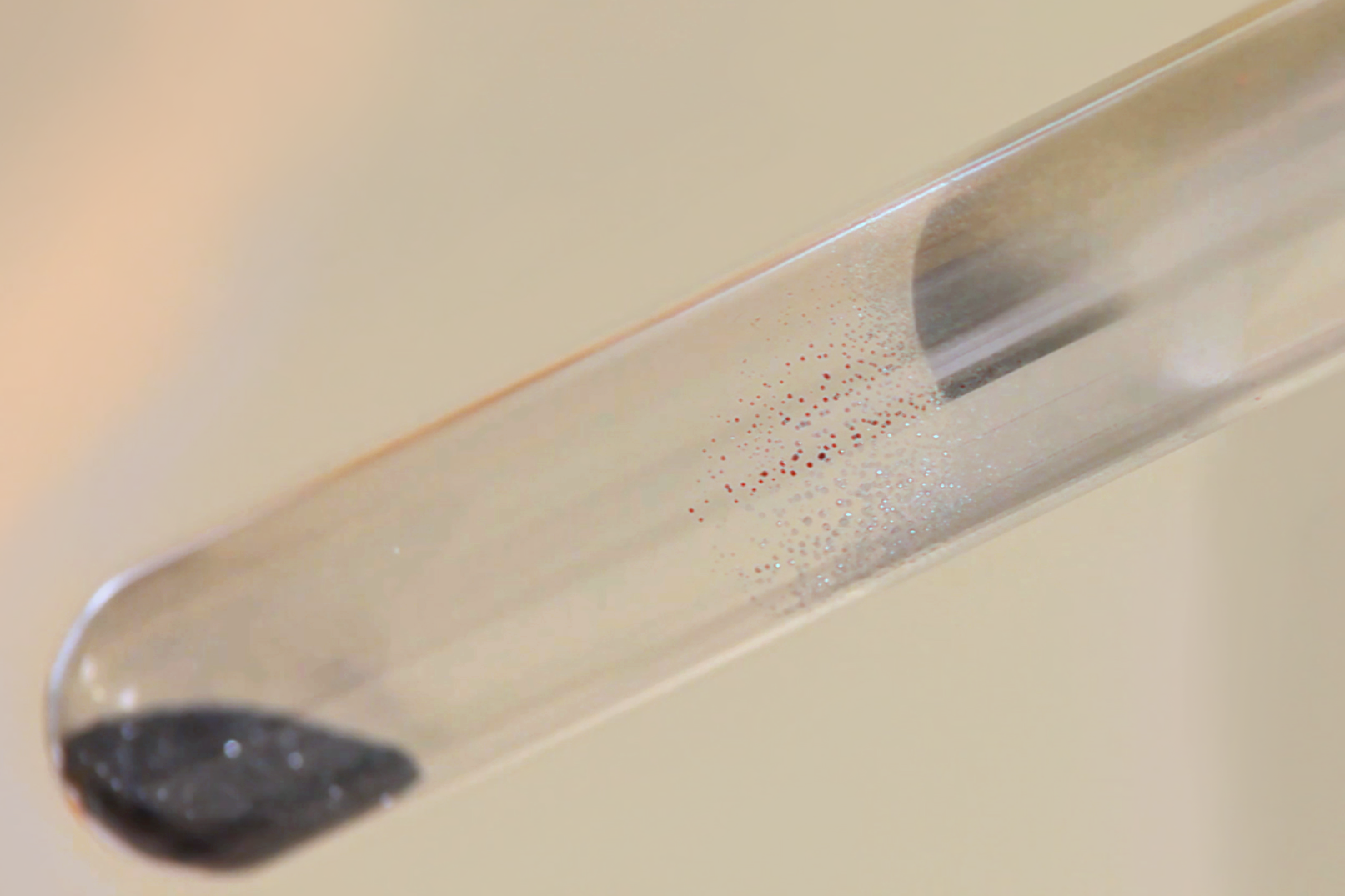 Zdjęcie zestawu do rozkładu tlenku rtęci dwa podczas pracy. Na zdjęciu widać rtęć osadzającą się w postaci maleńkich kropelek na ściankach probówki powyżej ogrzewanego ha gie o.