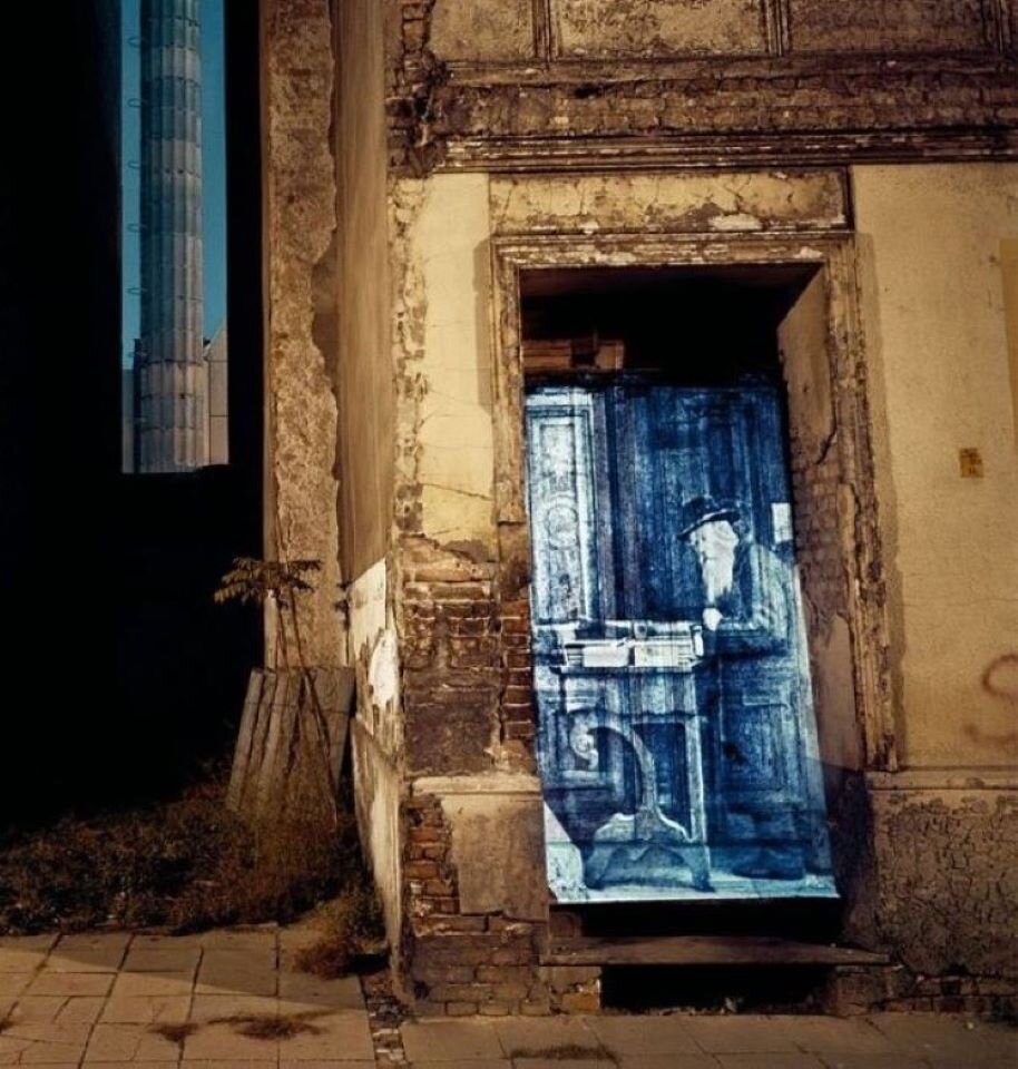 Ilustracja interaktywna przedstawia projekcję na dawnej księgarni żydowskiej w Berlinie. Po lewej stronie ukazany jest fragment bloku z płyty betonowej, parter i pierwsze piętro. Po prawej stronie fragment zniszczonego budynku, na drzwiach których ukazana została projekcja, przedstawiająca starszego żydowskiego mężczyznę, siedzącego przy biurku. W środku fotografii, w oddali, widoczny jest wysoki komin. Dodatkowo na ilustracji umieszczono następujące informacje: Podczas wizyty Berlinie w 1991 r. Attie szukał śladów kultury żydowskiej. Uderzyła go pustka pozostawiona po wymordowaniu mieszkańców Scheunenviertel. Dlatego wybrał fotografie wykonane przed II wojną światową, zamienił je na slajdy i projektował je bezpośrednio na fronty domów w kwartale.