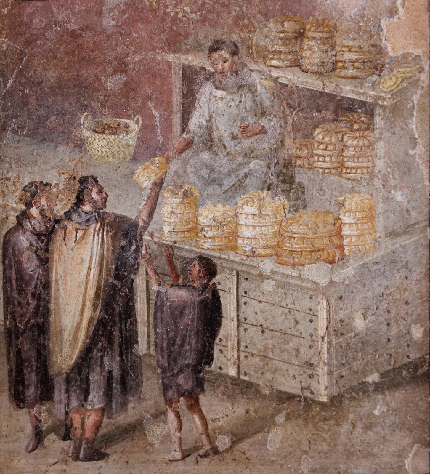 Ilustracja przedstawia fresk „Sprzedaż chleba w Pompejach” autora nieznanego. Obraz ukazuje piekarza, który sprzedaje chleb. Postać piekarza znajduje się za ladą, na której umieszczone są okrągłe bochenki chleba, jeden na drugim. Z tyłu, za postacią stoi szafa z półkami, na których również jest chleb. Przed ladą znajdują się trzy postaci - dwóch mężczyzn i jeden chłopiec. Środkowa postać bierze chleb od piekarza. Chłopiec z prawej strony unosi ręce ku górze chcąc dostać bochen. 