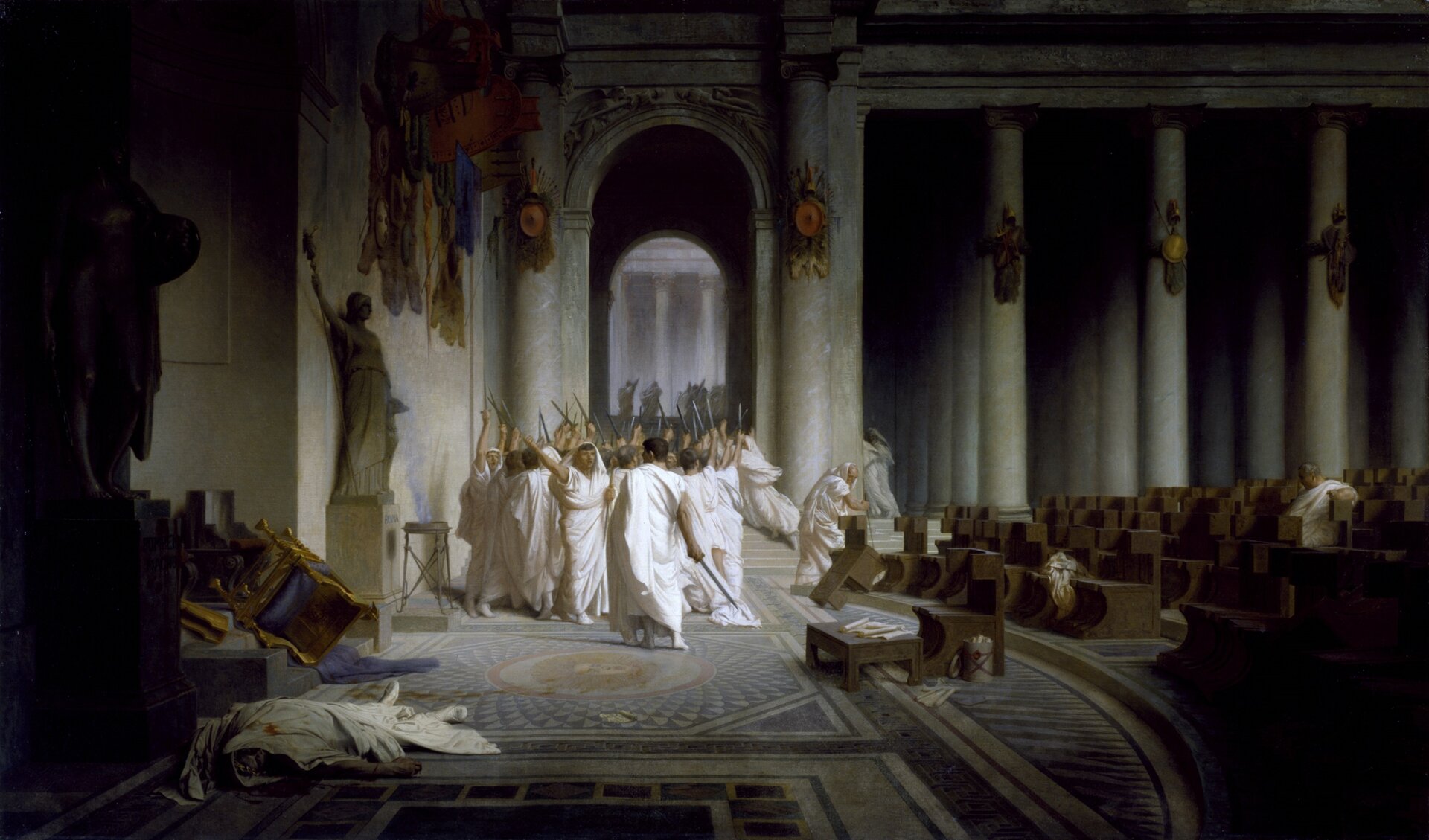 Ilustracja przedstawia obraz Jeana-Léona Gérômea „Śmierć Cezara”. Na obrazie znajduje się martwy mężczyzna w białych szatach, na których widać krew. W tle widoczni są inni ubrani na biało mężczyźni. Wszyscy mają ręce uniesione do góry. Postacie znajdują się w pomieszczeniu z licznymi ławkami, których część jest przewrócona. W oddali znajdują się także kolumny i wyjście z budynku. Nikt nie zwraca uwagi na martwego Cezara.