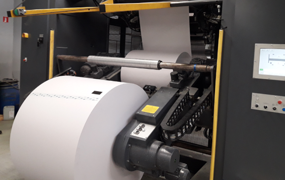 Na zdjęciu widoczna jest maszyna drukująca zwojowa typu zwój‑arkusz. Widoczne są dwa zwoje umieszczone jeden za drugim. Z boku urządzenia znajdują się przyciski do obsługi maszyny.