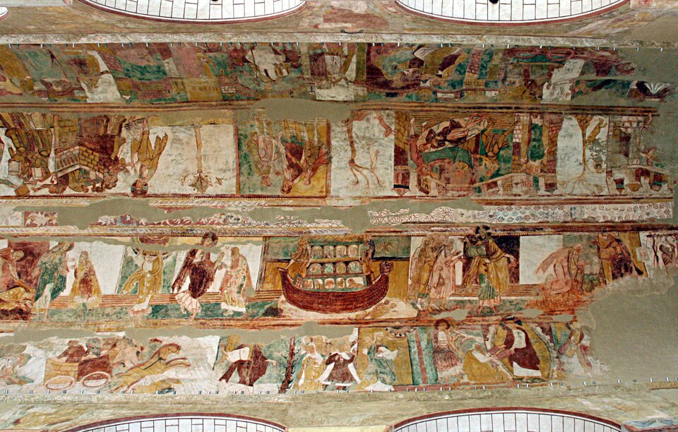 Sklepienie romańskiego kościoła pokryte rozległym cyklem średniowiecznych fresków, ułożonych w długie, poziome pasy narracyjne. Malowidła przedstawiają liczne sceny figuralne z postaciami ludzkimi, architekturą, zwierzętami i epizodami biblijnymi, rozmieszczone sekwencyjnie wzdłuż całej powierzchni sklepienia. Kolorystyka jest stonowana, z przewagą ochry, zieleni, czerwieni i błękitu; widoczne są ubytki tynku i fragmentaryczne zachowanie malowideł, podkreślające ich wiek i historyczny charakter.