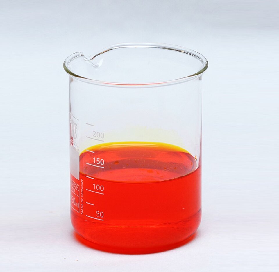 Zdjęcie przedstawia dużą zlewkę wypełnioną do połowy pomarańczową cieczą.