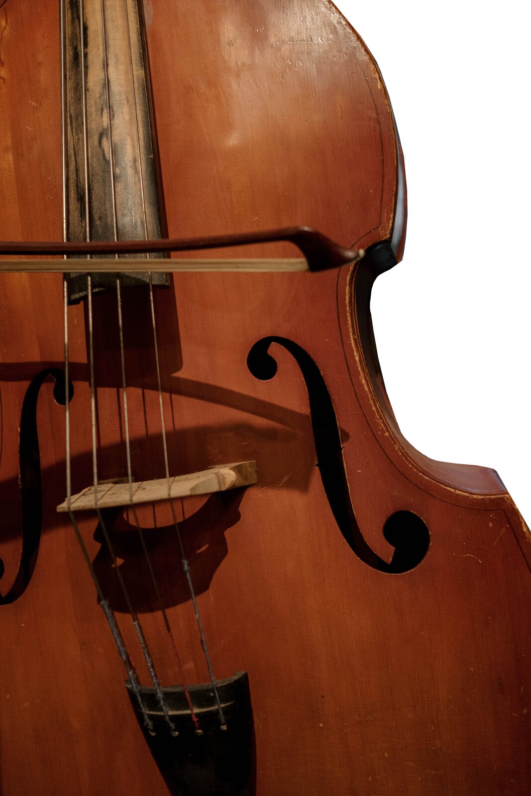 Na zdjęciu widoczny jest fragment pudła kontrabasu w kolorze brązowym z fragmentem czterech strun, na których poziomo spoczywa smyczek.