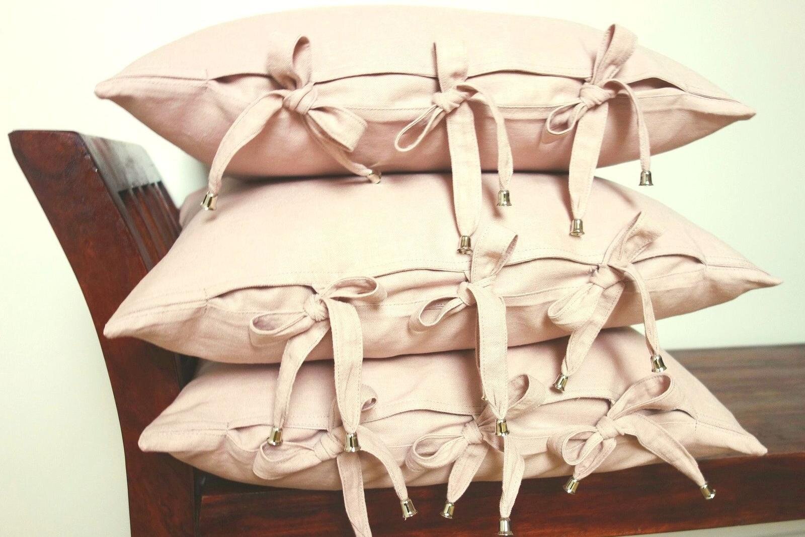 Ilustracja przedstawia poduszki w lnianych poszewkach. Poduszki poukładane są jedna na drugą , na bokach mają wiązania wykonane z tego samego materiału - po 3 liniane kokardki, których końce zakończone są metalowym dzwoneczkiem.