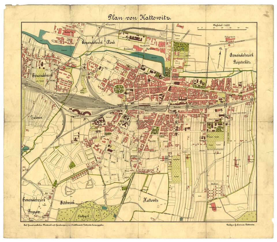Zdjęcie przedstawia starą, archiwalną mapę Katowic. Papier jest pożółkły, w wielu miejscach zabrudzony. Widoczne są ślady wskazująca na to, iż mapa była składana. U góry mapy znajduje się napis po niemiecku Plan von Kattowitz. Na mapie znajdują się oznaczenia w kolorach czerwonym (budynki), zielonym (miejskie tereny zielone),  czarnym (ulice, linie kolejowe). Widać też niewyraźne nazwy dzielnic.