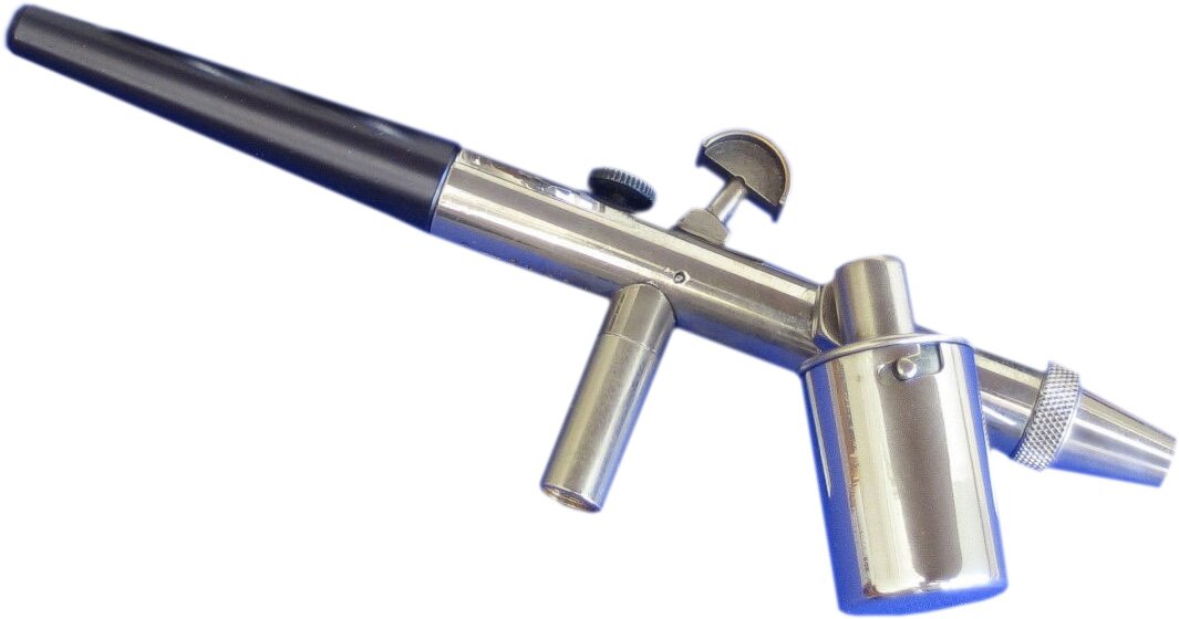 Zdjęcie przedstawia aerograf. Widoczne są korpus aerografu, cylindryczny zbiornik na farbę, zawór z grzybkowatym pokrętłem, cylindryczna dysz i prostopadle do niej, w jej połowie, usytuowana cylindryczna podpórka,
