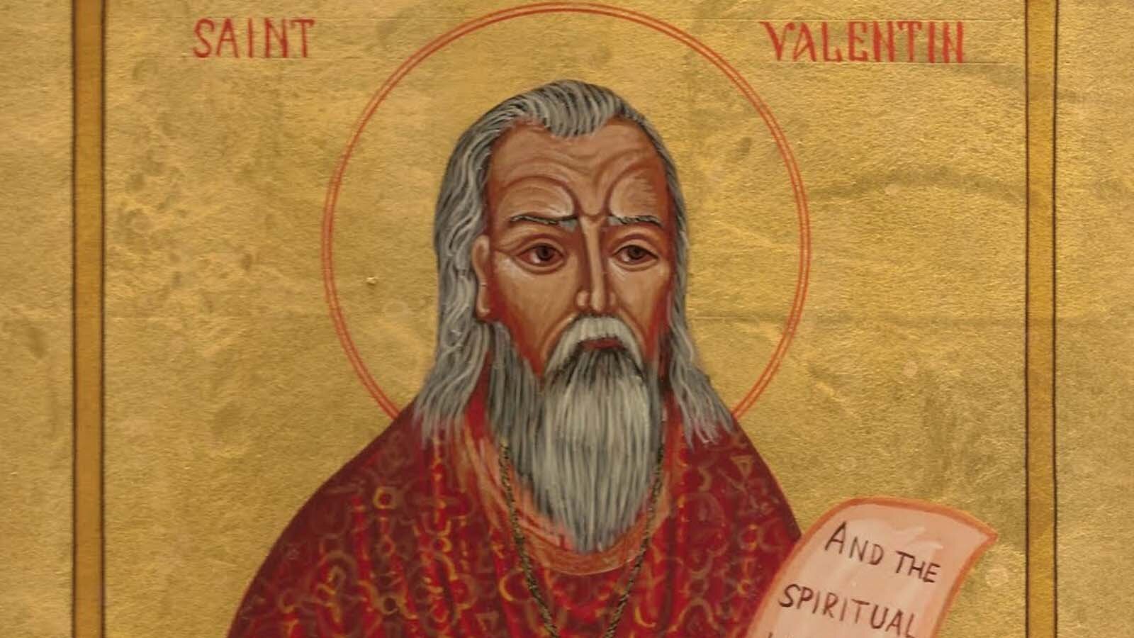 Zdjęcie przedstawia fragment ikony przedstawiającej świętego Walentego. U góry widoczny jest napis z czerwonych liter: SAINT VALENTIN. Na złotym tle przedstawiony jest starszy mężczyzna z półdługimi, siwymi włosami, siwą brodą i wąsami. Na jego twarzy, zwróconej lekko w prawo, widoczne są głębokie zmarszczki, a wokół głowy widoczna jest czerwona aureola. Święty ubrany jest w czerwony ornat ze złotym wzorem. Po prawej stronie widoczny jest fragment papieru, na którym widać słowa w języku angielskim: AND THE SPIRITUAL.