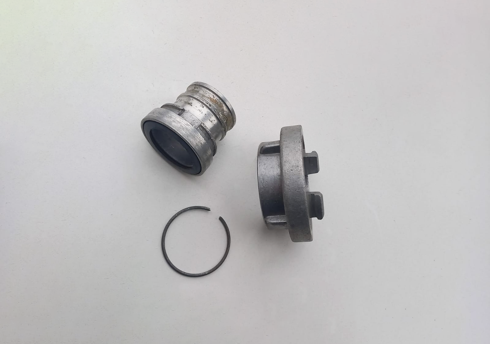 Zdjęcie przedstawia dwa łączniki. Łącznik z prawej strony ma większą średnicę i jest płaski. Łącznik z lewej strony przedstawiony jest z profilu, ma mniejszą średnicę i jest wyższy. Widoczny jest element łącznika, na który zakładany jest wąż. 