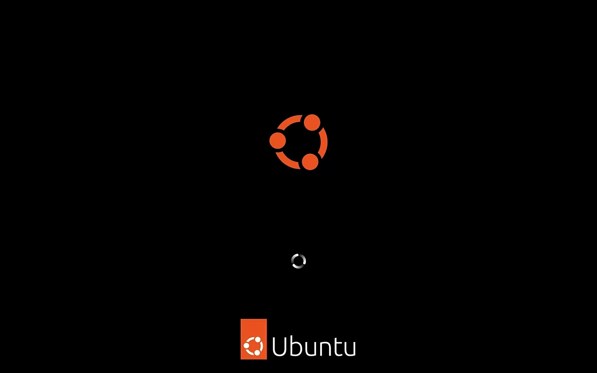 Na zdjęciu pokazano ekran powitalny dla systemy: Ubuntu 23.04. W dolnej części, na dole ekranu na czarnym tle znajduje się napis: Ubuntu. W centralnej części ekranu widoczny jest symbol. Symbol jest w kształcie pomarańczowego okręgu z wpisanym w środku okręgiem zbudowanym z trzech identycznych niepołączonych ze sobą łuków. Nad każdym z łuków w połowie jego długości znajduje się kropka.